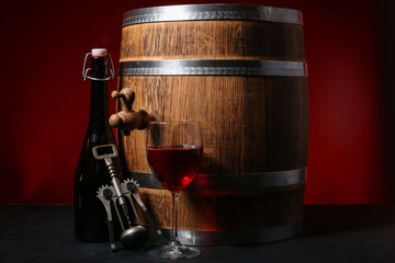 Obraz premium Wooden barrel, corkscrew, bottle and glass of wine on dark background