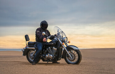 Obraz premium Exclusive Image: Off-road motorcyclist riding through the vast Namib Desert at golden hour, framed by sweeping sand dunes and a dramatic cloudy sky. A powerful scene of freedom, adventure travel