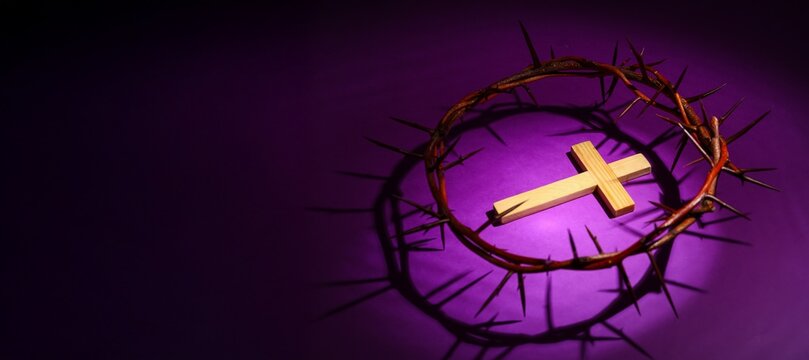 Wooden cross with crown of thorns on dark purple background with space for text