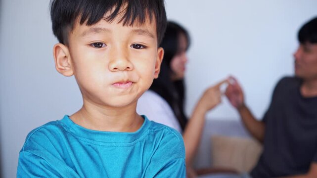 Focused sad ittle boy  while his parents are arguing in the background. Concept of family conflict, divorce, domestic problems, and the emotional impact on children's mental health.