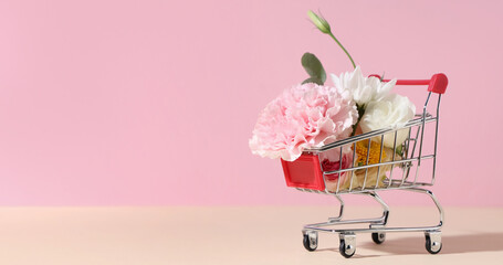 Small shopping cart with beautiful flowers on color background © Pixel-Shot