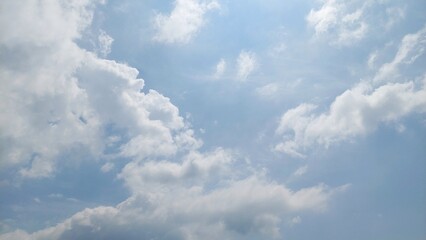 Fototapeta premium Clear blue sky with floating white clouds. Natural sky background in bright summer daylight. Beautiful blue sky texture with cloud formations.