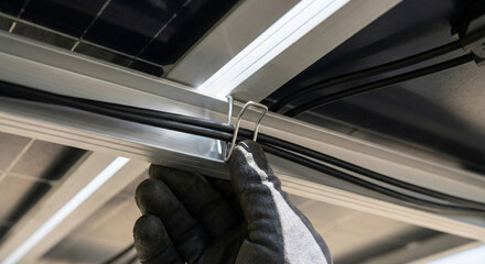 Obraz premium Technician securing solar cables with metal clip under panel frame