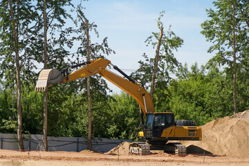 A new yellow excavator stands on a construction site with its boom raised next to a pile of sand. © Борис Бондарчук