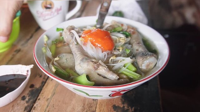 Adding sambal to the Mie Bakso (meatballs) with vermicelli, vegetables, and chicken feet at a stall. This is one of the most favorite street food in Indonesia on June 28, 2025 in Bandung, Indonesia