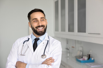 Medical achievements and optimism. Smiling confident handsome male doctor pose in hospital office or laboratory workplace with crossed arms look at distance visualize professional success. Copy space