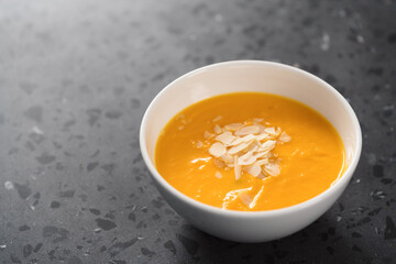 Pumpkin soup puree decorated with almond flakes in white bowl on concrete background