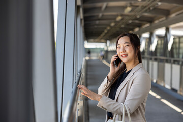 Fototapeta premium Luxury young Asian CEO woman entrepreneur using mobile phone while walking in the urban skyscraper street modern office downtown on background for business communication and urban lifestyle concept