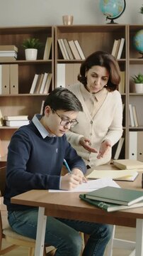 Teacher guiding a student with his assignment at a desk in a well-organized study room, vertical shot