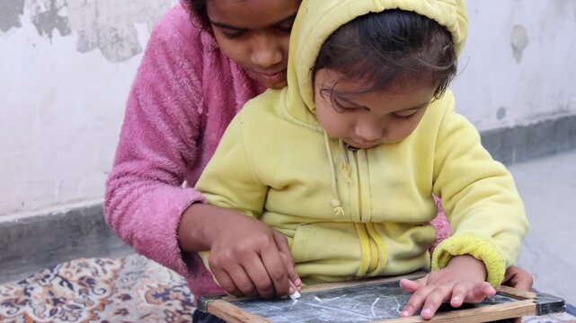 Caring elder sister from a rural village in Uttarakhand, India, teaching her younger sibling to write on a chalkboard at home, showcasing education, bonding, and simple mountain village life.