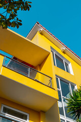 Vibrant yellow modern home with clear blue sky and tropical foliage
