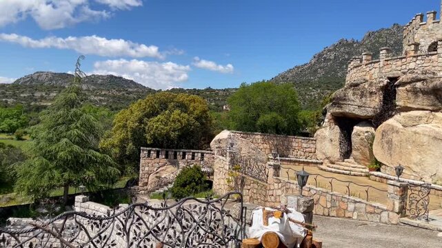 Stone castle built into natural rock formations in the La Cabrera mountain range near Madrid, Spain, surrounded by rugged landscape and blue sky, representing history, architecture, and rural travel i