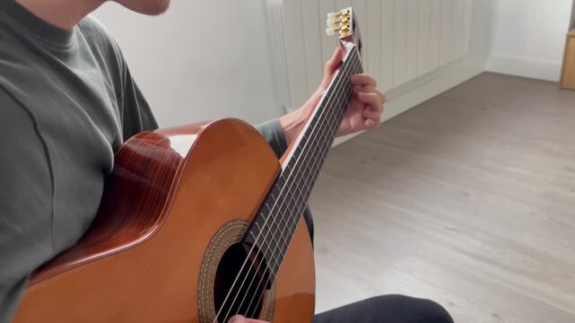 Man practicing classical guitar at home during an online music lesson. Adult musician learning and improving technique through remote education and self-study. Online learning platforms concept