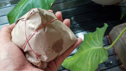 Hand Holding Traditional Indonesian Nasi Bungkus Wrapped in Brown Paper