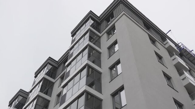 High-rise building with strict facade combines residential complex and office center. Monolithic gray tower reflects modern city lifestyle
