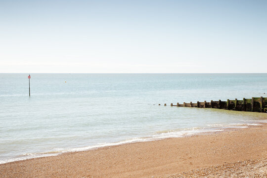 Tranquil Beach Scene With Calm Sea, Wooden Jetty, And Clear Horizon Under Blue Sky