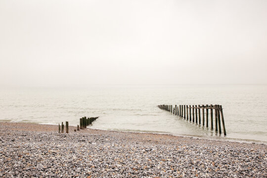 Misty Seaside Pier Extending Into Calm Grey Ocean Across Pebble Beach, Winter Mood