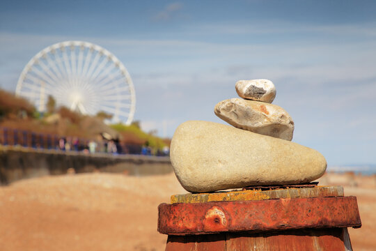 Balanced Stone Stack On Beach With Ferris Wheel In Background Under Sunny Sky
