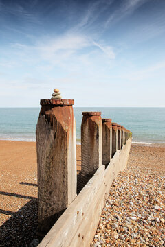 Coastal Wooden Breakwater With Stacked Stones on Pebble Beach Under Clear Blue Sky