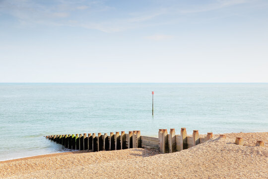 Calm Sea With Wooden Groynes Along Pebble Beach Under Clear Blue Sky