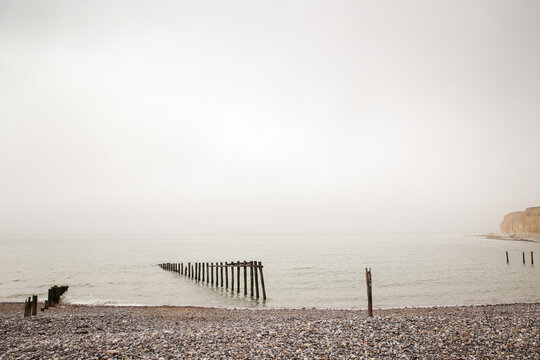 Moody Coastal Scene With Abandoned Pier Posts On Pebble Beach At Dusk