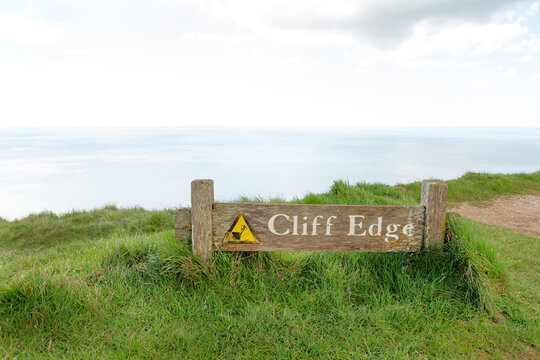 Cliff Edge Sign On a Rugged Coastline With Open Ocean View and Grass-Cilled Path