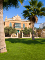 Malta, Marsaxlokk &ndash; Mediterranean park with palm trees, lawn and view of baroque mansion with balustrade and shutters