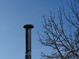Obraz premium Snow covered old metal chimney and tree branches against a blue sky.