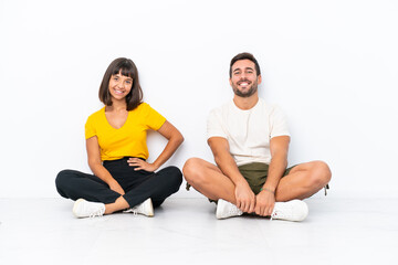 Fototapeta premium Young couple sitting on the floor isolated on white background posing with arms at hip and smiling