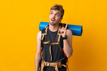 Young mountaineer man with a big backpack isolated on yellow background thinking an idea pointing...