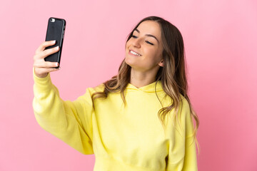 Fototapeta premium Young Romanian woman isolated on pink background making a selfie with mobile phone