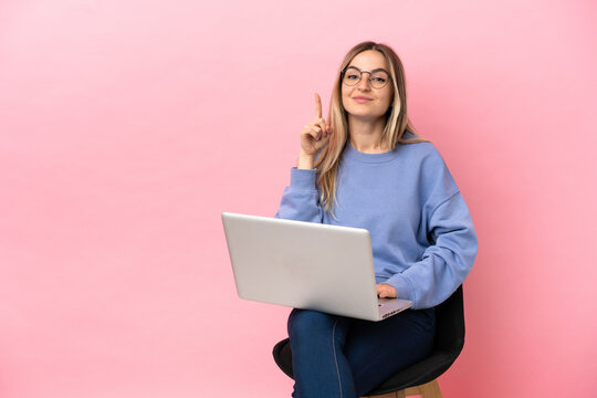 Young woman sitting on a chair with laptop over isolated pink background pointing with the index finger a great idea
