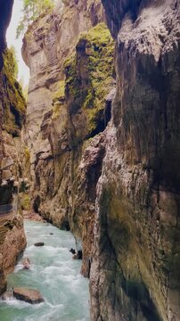spring river flowing through the narrow rocky partnach gorge. water dripping from above creates a fairy tale atmosphere, with dramatic cliffs and a narrow rock path where tourists are walking.garmisch