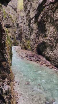 spring river flowing through the narrow rocky partnach gorge. water dripping from above creates a fairy tale atmosphere, with dramatic cliffs and a narrow rock path where tourists are walking.garmisch