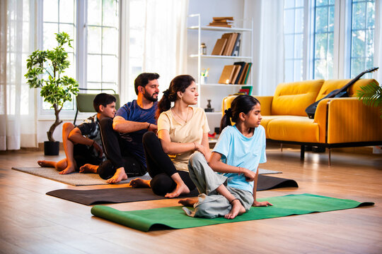 Indian parents and children performing seated spinal twist yoga together indoors
