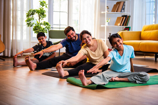 Indian parents and children performing seated head to knee yoga together indoors