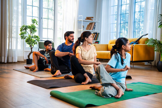 Indian parents and children performing seated spinal twist yoga together indoors