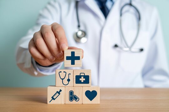 Doctor's hand placing medical cross cube on stack of healthcare symbols blocks