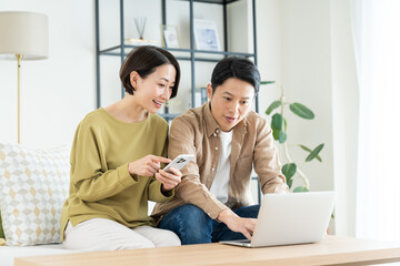 リビングでスマホとパソコンを使うミドルの夫婦