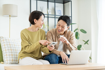 リビングでスマホとパソコンを使うミドルの夫婦