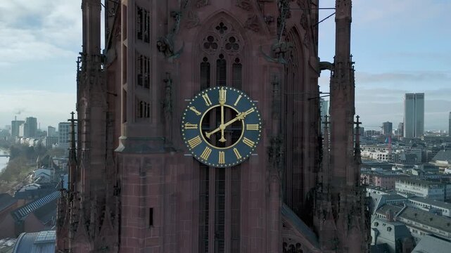 Aerial drone footage of Frankfurt Cathedral featuring a close view of the clock tower and moving clock hands. Captured on a clear, sunny winter day at midday, highlighting historic architecture agains