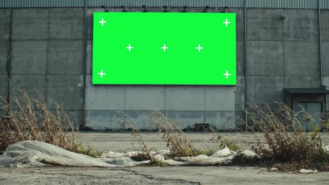 Outdoor video green screen display on concrete wall with dry plants surrounding it, interactive green screen video setup