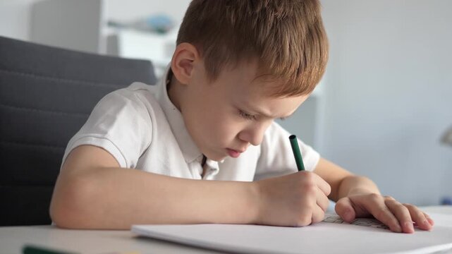 Close-up of a young boy writing or drawing with a pencil at a desk at home or school. Child focused on learning and doing homework. Concept of education, childhood development, concentration
