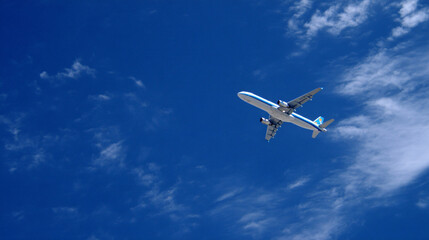 Fototapeta premium An airplane flying through a blue sky with scattered clouds.