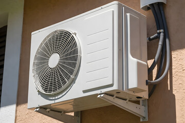 Fototapeta premium A white air conditioning unit mounted on a brown stucco wall with gray tubes and wires