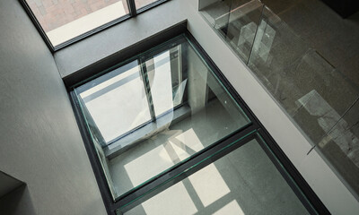 Fototapeta premium Glass architecture floor view looking down through a transparent walk on panel from an upper story in a modern minimalist building