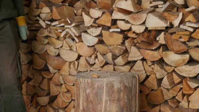 Person with face not visible using an axe to split a wooden log on a chopping block for fireplace fuel preparation