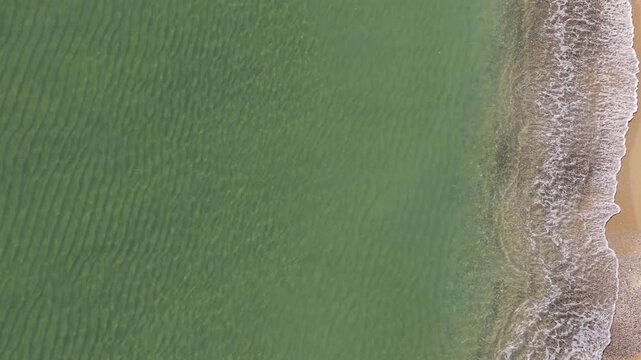 Drone footage shows emerald ocean surface and rocky edge with soft waves forming abstract coastline pattern calm
