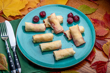 Fototapeta premium Enjoying dessert rolls on a blue plate. A group of dessert rolls sits on a blue plate with grapes. Colorful leaves surround the plate and cutlery.
