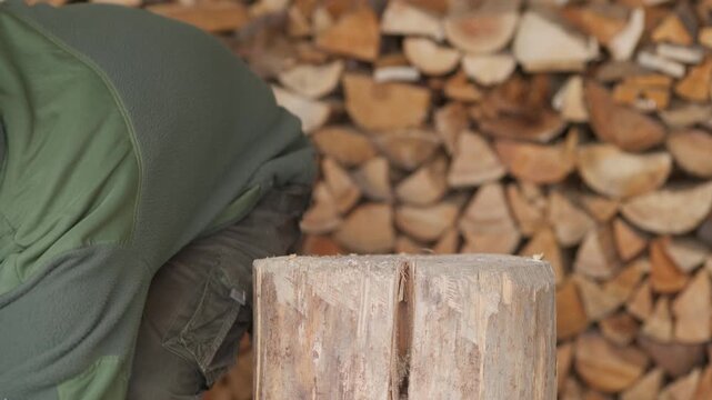 Side view of hands using an axe to split a wooden log on a chopping block to prepare fuel for a fireplace